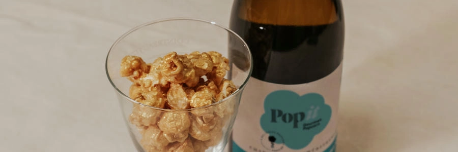 Copa con palomitas gourmet Popit frente a una botella de vino: acompañamiento perfecto