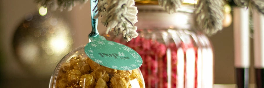 Bola navideña transparente con palomitas Popit y etiqueta turquesa colgada del árbol