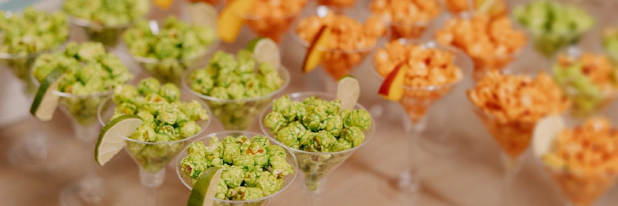 Copas tipo cóctel con palomitas gourmet Popit verdes y naranjas en barra de degustación para eventos