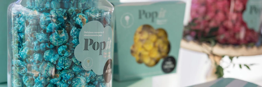 Tarro de palomitas gourmet Popit color turquesa con packaging de la marca al fondo, ideal como regalo corporativo
